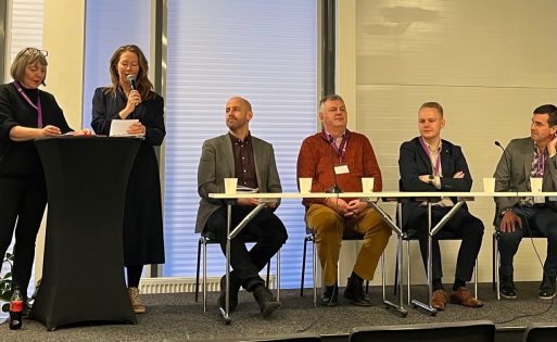 Två personer står framme vid ett podium tillsammans med fyra sittande personer i en panel